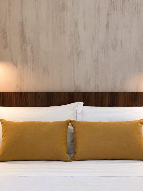 Letto Suite Terra Eden con cuscini dorati, testata in legno e pareti imbiancate presso l'hotel boutique Domus Fysi a Palermo