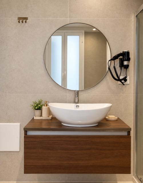 Bagno moderno di Domus Fysi B&B Palermo con specchio rotondo, lavabo bianco, mobile in legno e piastrelle beige