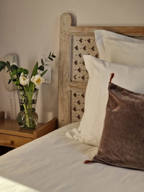 Chambre confortable à l'Hôtel Les Lauriers avec oreillers blancs, coussin marron, fleurs fraîches et tête de lit rustique en bois