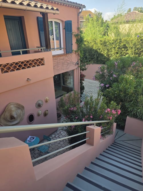 Cour de l'Hôtel Les Lauriers à Saint-Tropez avec murs en terre cuite, fleurs roses, escaliers rayés et jardin méditerranéen
