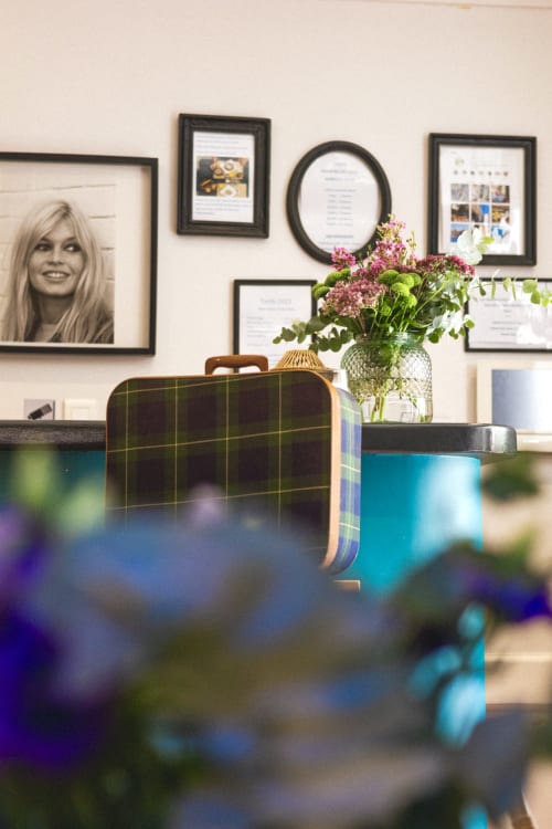 Le hall de l'Hôtel Les Lauriers à Saint-Tropez présente des photos encadrées, un mur galerie, des valises vintage et des fleurs fraîches