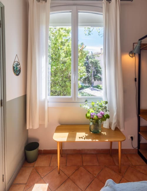 Chambre lumineuse aux Lauriers, Saint-Tropez, avec bureau en bois, fleurs et vue sur le jardin par les portes-fenêtres