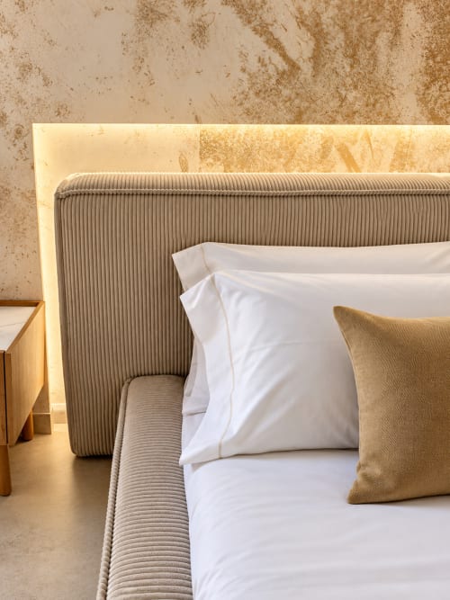 Letto moderno con testata a righe, biancheria bianca e cuscino beige nella suite Palermo con illuminazione ambientale