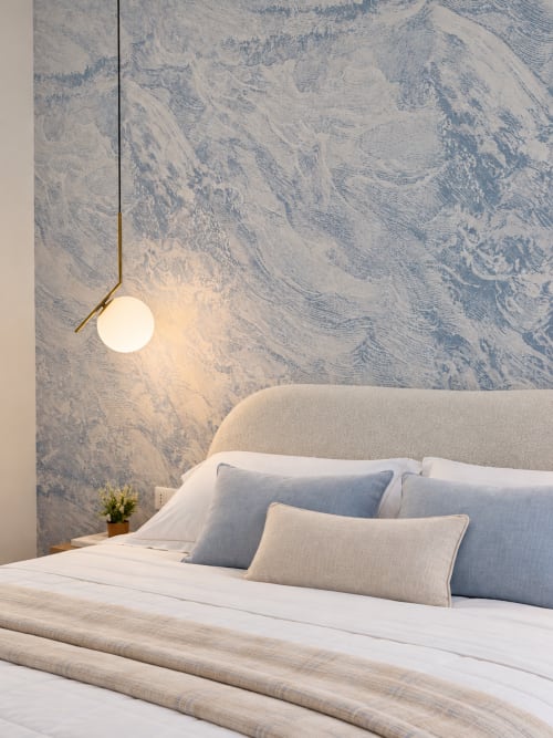 Camera moderna a Domus Fysi Palermo con testata curva beige, cuscini blu, lampada a sospensione e pareti blu-grigio texturizzate