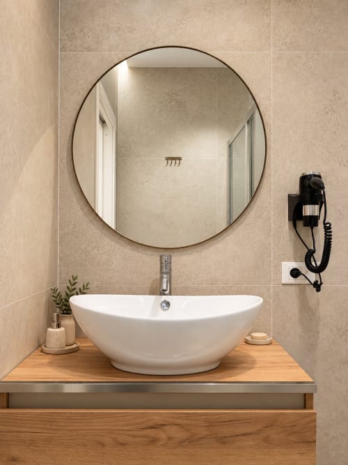 Lavabo moderno con specchio rotondo presso la suite Domus Fysi a Palermo, con vasca bianca e vanità in legno