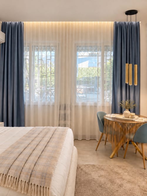 Suite elegante a Domus Fysi Palermo con letto, tavolo da pranzo, tende grigie e accesso a balcone con vista sulla città