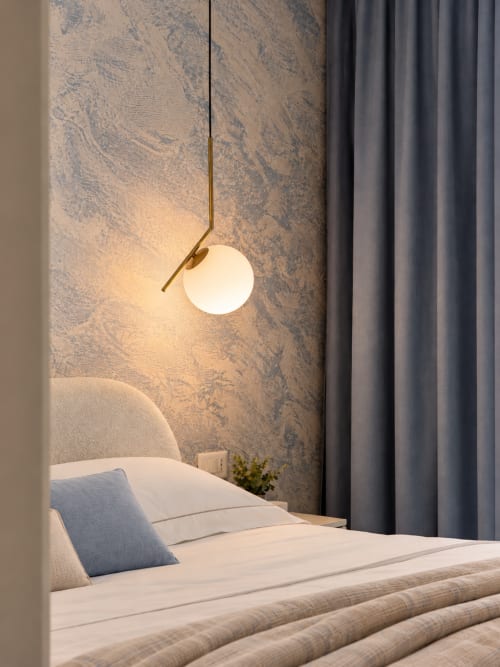 Camera moderna a Domus Fysi Palermo con lampada a sospensione sopra il letto, carta da parati a motivi e tende grigie