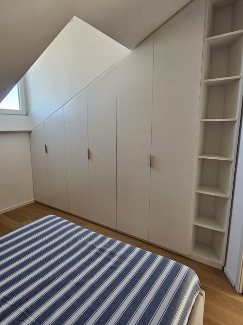 Camera da letto in mansarda moderna con armadi bianchi incorporati, scaffali aperti e biancheria a righe presso Pescara INN