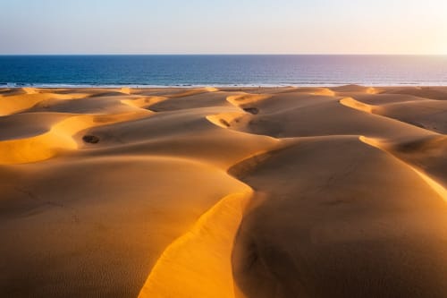 Dunas de arena dorada se encuentran con el océano turquesa al atardecer cerca de Arucas, Las Palmas - escapada costera ideal para huéspedes del hostal MBM