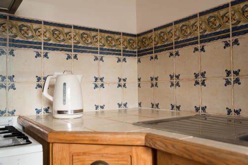 Coin cuisine au Domaine Chapelle avec carrelage bleu décoratif en crédence et bouilloire blanche sur comptoir en bois