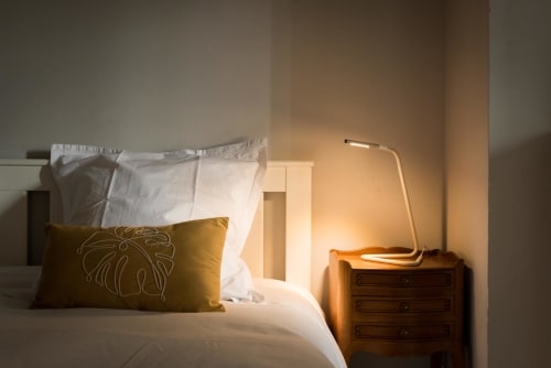 Chambre douillette au Domaine Chapelle B&B avec oreiller doré, literie blanche, table de nuit en bois et lampe moderne