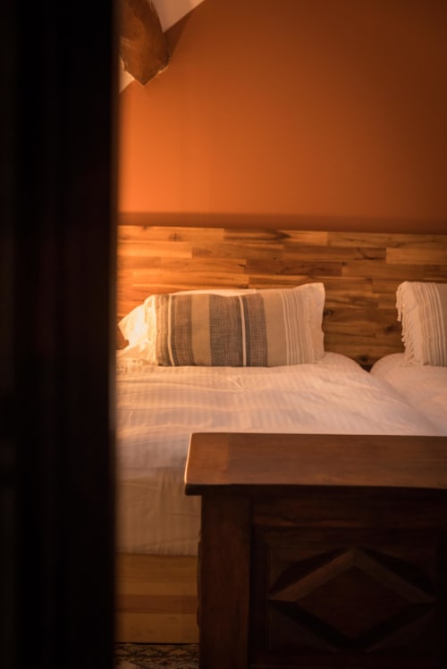 La lumière dorée du coucher de soleil inonde une chambre confortable au Domaine Chapelle avec parquet, linge blanc et oreillers rayés.