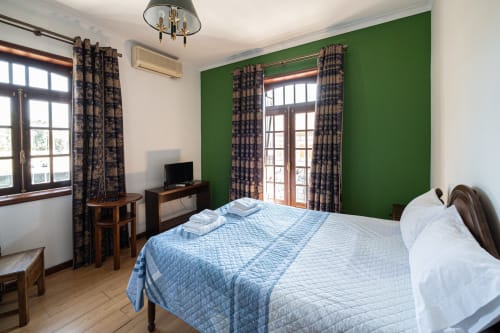 Quarto luminoso na Casa Augusta hostel com cama queen, parede verde de destaque, móveis de madeira e portas para o jardim em Penafiel,