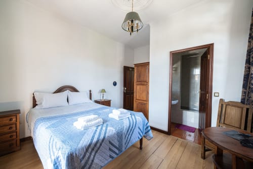 Quarto luminoso com cama de madeira, colcha acolchoada azul, móveis de madeira e banheiro privativo na Casa Augusta
