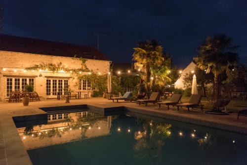 Domaine Chapelle nighttime pool area with lounge chairs, palm trees, and illuminated stone building in La Chapelle-la-Reine,