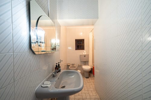 Banheiro moderno da pousada Casa Augusta em Penafiel com paredes de azulejo branco, pia, vaso sanitário e espelho com iluminação