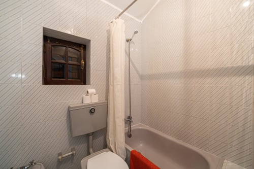 Banheiro moderno com azulejos subway brancos, vaso sanitário, banheira com chuveiro e pequena janela na pousada Casa Augusta em Penafiel