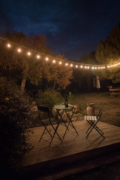 Terrasse du Domaine Chapelle au coucher du soleil avec guirlandes lumineuses, terrasse en bois, chaises de bistrot et bouteille de vin avec vue sur la campagne française