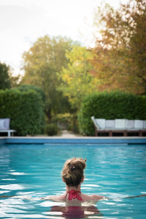 Femme se relaxant dans la piscine extérieure du Domaine Chapelle, un gîte en Vallée de la Reine, entourée de haies