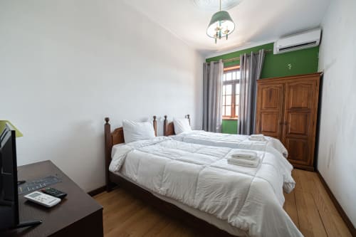 Suíte duplo luminosa na Casa Augusta Penafiel com cama de madeira, parede de destaque em verde e vista da cidade através de grandes janelas