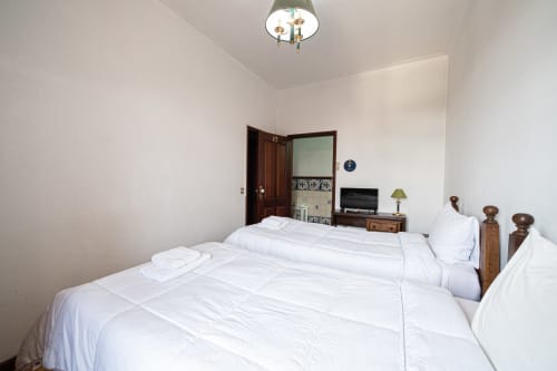 Luminoso quarto duplo da suíte na pousada Casa Augusta em Penafiel, com roupa de cama branca, móveis de madeira e vista da cidade.