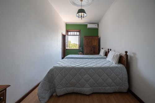 Quarto iluminado na hospedaria Casa Augusta em Penafiel com cama queen, parede verde destaque, móveis de madeira e luz natural