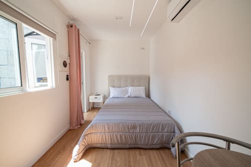 Quarto moderno da pousada Casa Augusta com cama de solteiro, roupa de cama cinza, piso de madeira, cortinas rosa e