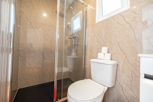 Banheiro moderno da pousada Casa Augusta em Braga com azulejos de mármore bege, box de vidro e vaso sanitário branco