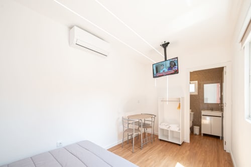 Quarto moderno da Casa Augusta com cama, mesa de jantar, TV, ar condicionado e banheiro privativo com pia visível