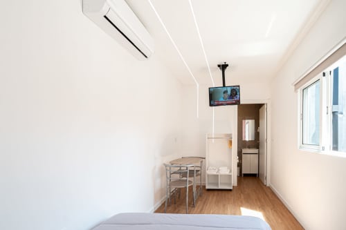 Quarto compacto na pousada Casa Augusta em Braga com cama, mesa de refeições, TV, banheiro e piso de madeira