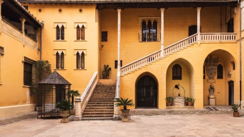 Patio de las Casa Rural Garden Suites en Xàtiva con edificio de piedra amarilla, pórtico abovedado y escalinata principal