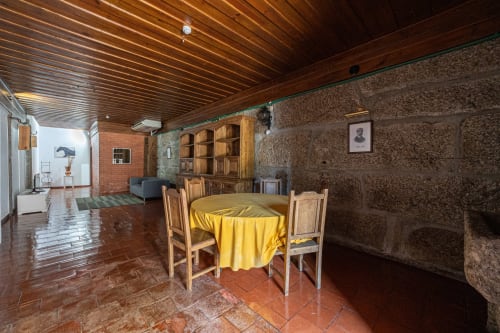 Sala de refeições do hostel Casa Augusta com mesa redonda amarela, cadeiras de madeira, paredes de pedra aparente e teto de madeira em Penafiel,