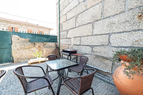 Área de estar ao ar livre da pousada Casa Augusta em Penafiel com cadeiras de vime, paredes de pedra e plantas em vasos