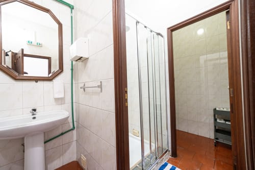 Banheiro da Suite Familiar na pousada Casa Augusta em Penafiel com azulejos brancos, pia coluna, espelho e chuveiro