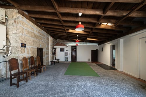 Área comum do hostel Casa Augusta em Braga, Portugal com vigas de madeira, paredes de pedra, campo de minigolfe verde e vermelho