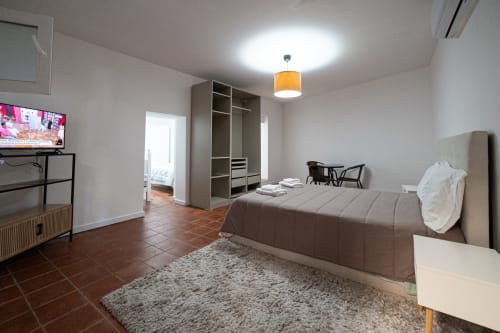 Quarto espaçoso da pousada Casa Augusta em Braga, com cama, guarda-roupa, TV, piso em terracota e comodidades modernas
