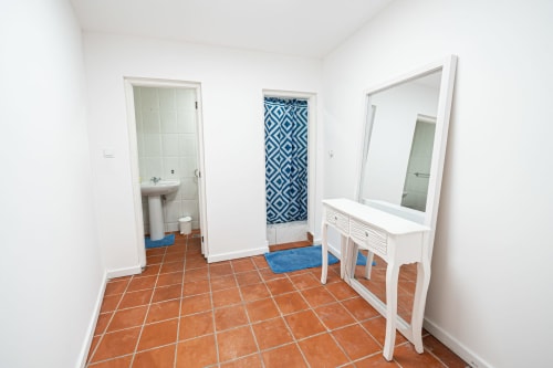 Quarto C5 do hostel Casa Augusta com piso de telha, bacia branca, espelho grande e porta azul do banheiro em Braga, Portugal