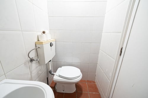 Banheiro pequeno no Quarto C5 da pousada Casa Augusta, Braga, com paredes de azulejos brancos, vaso sanitário, pia e piso com azulejos vermelhos.
