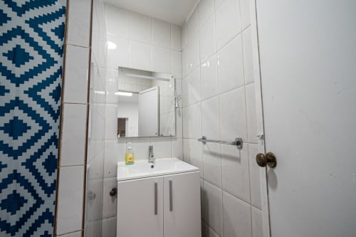 Casa Augusta em Braga: banheiro moderno com azulejos brancos, pia, espelho e cortina de chuveiro geométrica azul