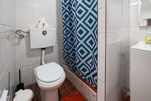 Casa Augusta hostel - banheiro em Braga, Portugal com azulejos brancos, vaso sanitário, pia e cortina de chuveiro com padrão azul