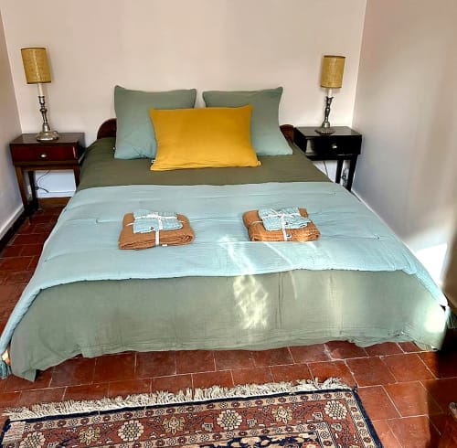 Chambre élégante aux Maraîchades avec literie verte, oreiller jaune, lampes jumelées et sols en terre cuite