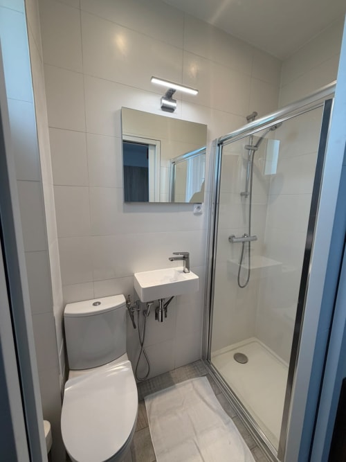 Salle de bain moderne à l'Hôtel le Dellys à Colombes avec toilettes, lavabo, miroir et douche fermée