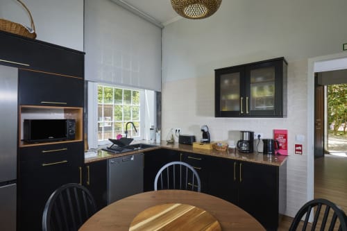 Cozinha de chalé moderno com armários pretos, bancadas em granito, eletrodomésticos em aço inoxidável e mesa de jantar com vista para o lago