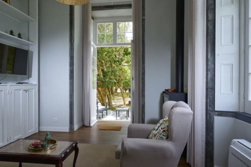 Sala luminosa com poltrona cinza, mesa de madeira, TV de tela plana e portas francesas com vista para o lago das Furnas na Casa Dos