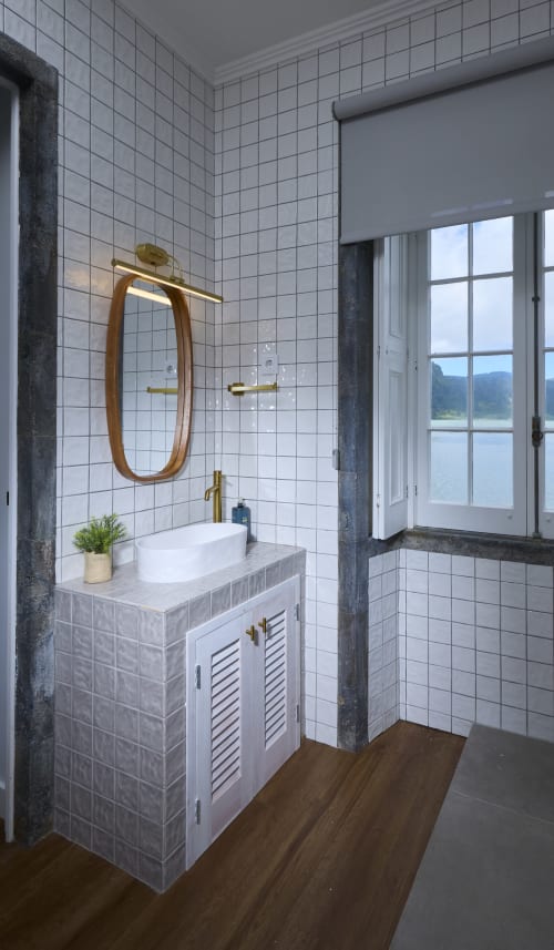 Banheiro moderno com azulejos brancos, louças em latão, espelho oval e janela com vista para o lago na casa de hóspedes Casa Dos Barcos Furnas