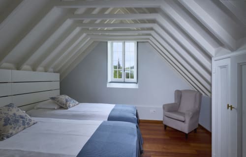 Quarto aconchegante na mansarda da Casa Dos Barcos em Furnas, com vigas aparentes, camas de solteiro, poltrona e vista para o lago