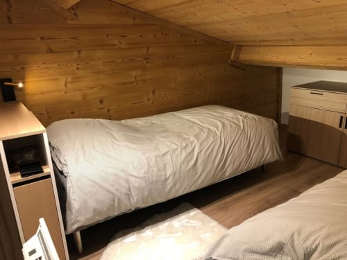 Chambre cosy en mezzanine aux Tanières de Montgenèvre : poutres en bois, lit simple et vue montagne.