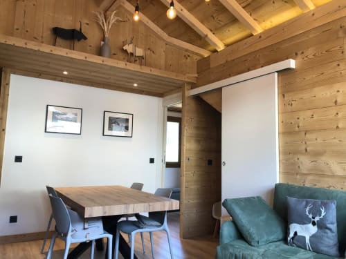 Intérieur d'appartement alpin moderne avec poutres en bois, table à manger, canapé vert et vue sur les montagnes aux Tanières de