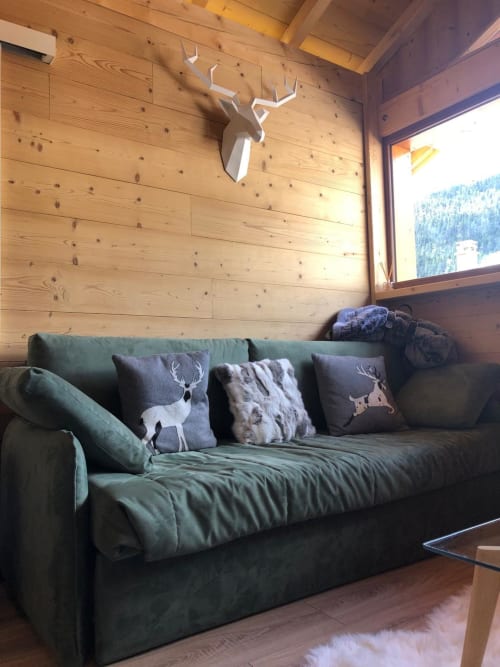 Salon alpin cosy aux Tanières de Montgenèvre avec canapé vert, coussins à motifs de cerfs, murs en bois et vue montagne