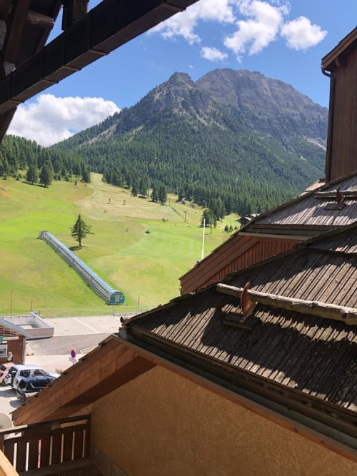 Vue montagne depuis le balcon de l'appartement Les Tanières de Montgenèvre, pentes vertes et remontée mécanique visibles